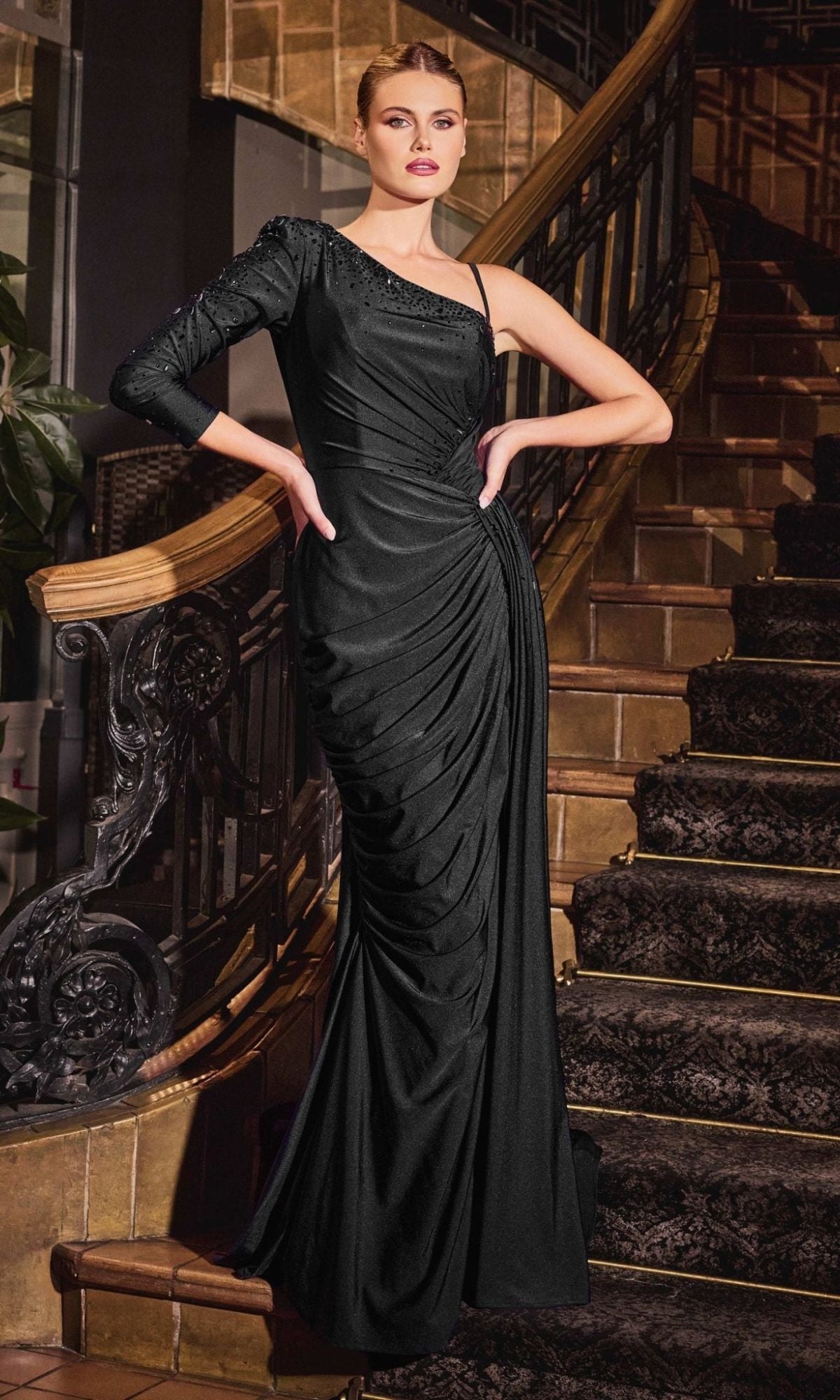 A woman stands on a staircase wearing the Ladivine CD787 One-Sleeve Long Formal Dress—a black, asymmetrical gown with ruched detailing, perfect for elegant evenings and special occasions.